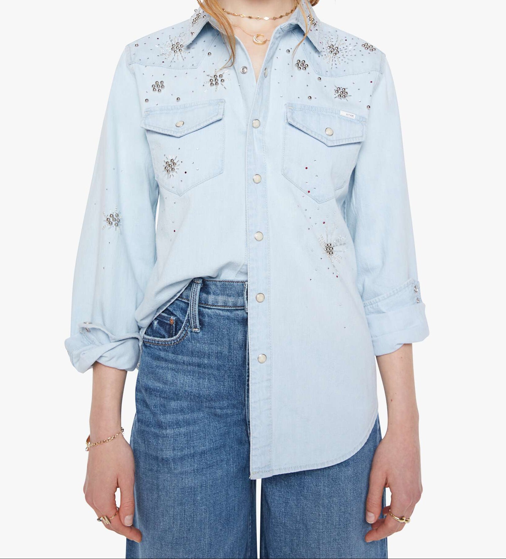 Woman wearing a light blue denim shirt with embellishments on a white background