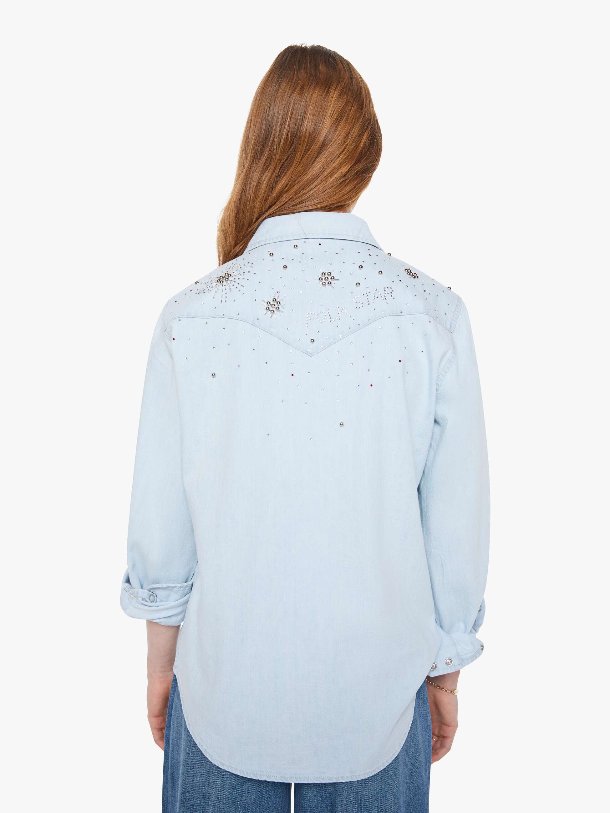 Woman wearing a light blue denim shirt with floral embroidery on a white background