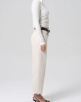 Person wearing a white long-sleeve top and beige pants on a plain background