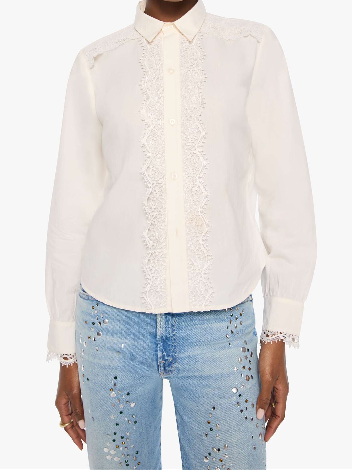 A model wearing a white long-sleeve button-up blouse with delicate lace trim down the front and on the shoulders, paired with light blue jeans featuring sequin embellishments, set against a plain white background.