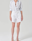 Person wearing a light gray button-up shirt and white shorts on a plain background