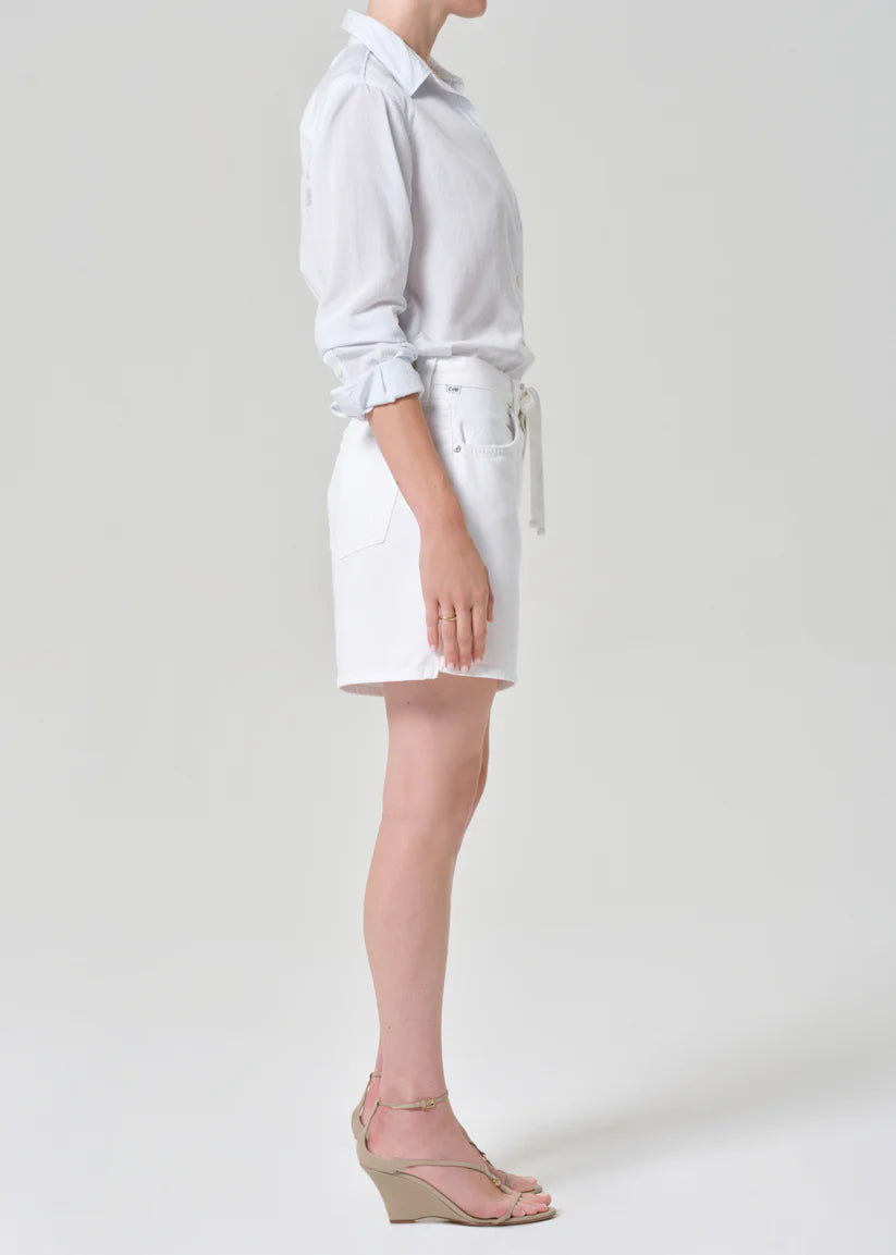 Person wearing a light gray shirt and white shorts on a plain background