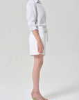 Person wearing a light gray shirt and white shorts on a plain background
