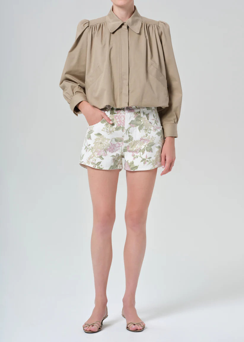 Person wearing a beige blouse and floral shorts on a white background