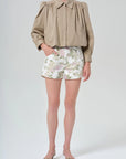 Person wearing a beige blouse and floral shorts on a white background