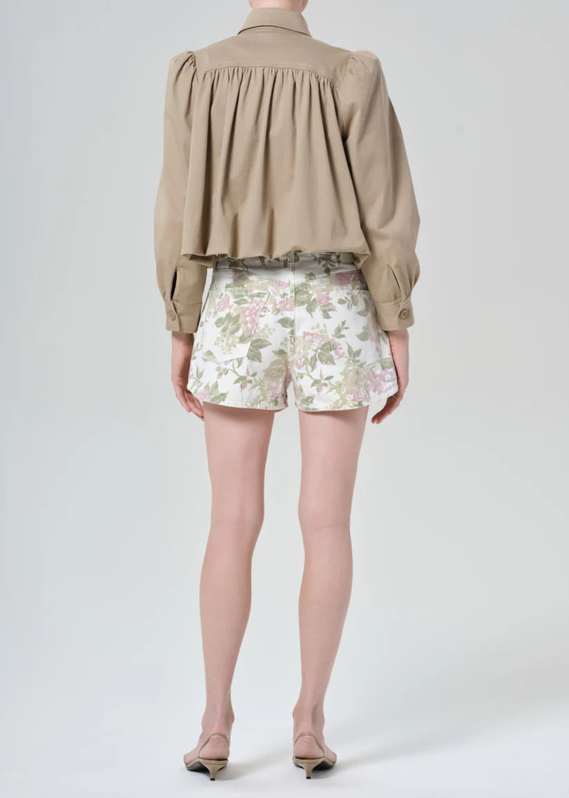Person wearing a beige shirt and floral shorts on a white background