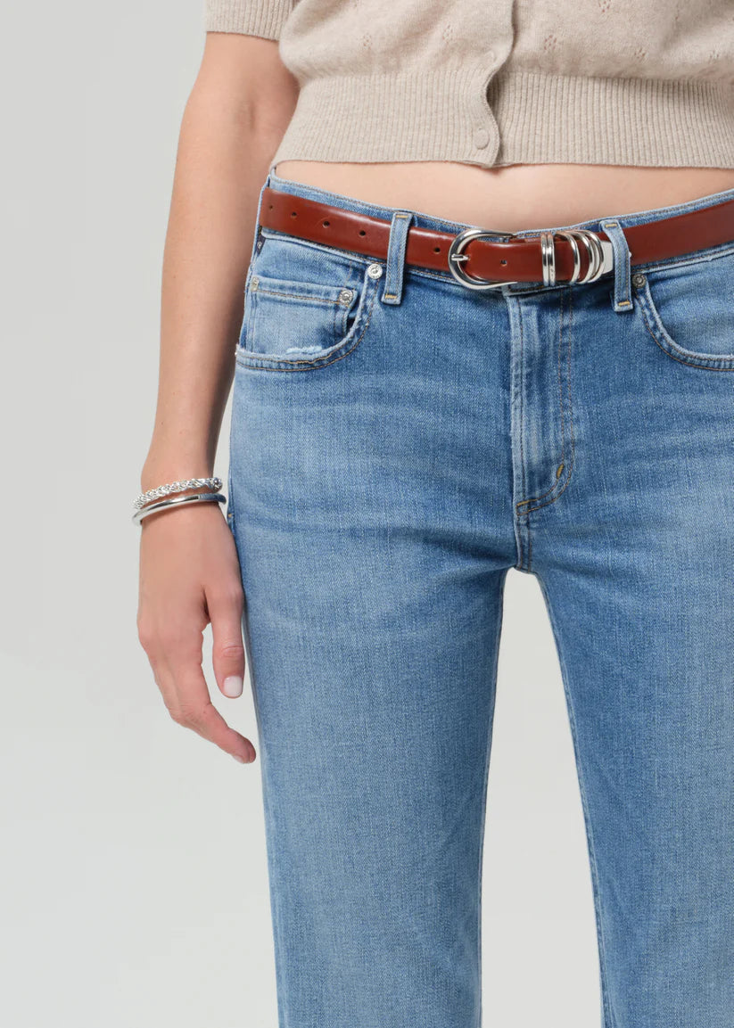 Person wearing blue jeans with a brown belt on a light gray background