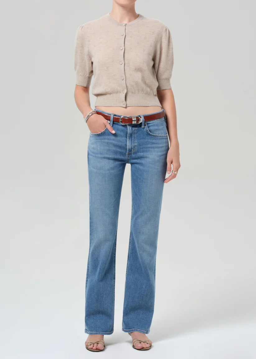 Person wearing a beige cardigan, blue jeans, and a brown belt on a light gray background