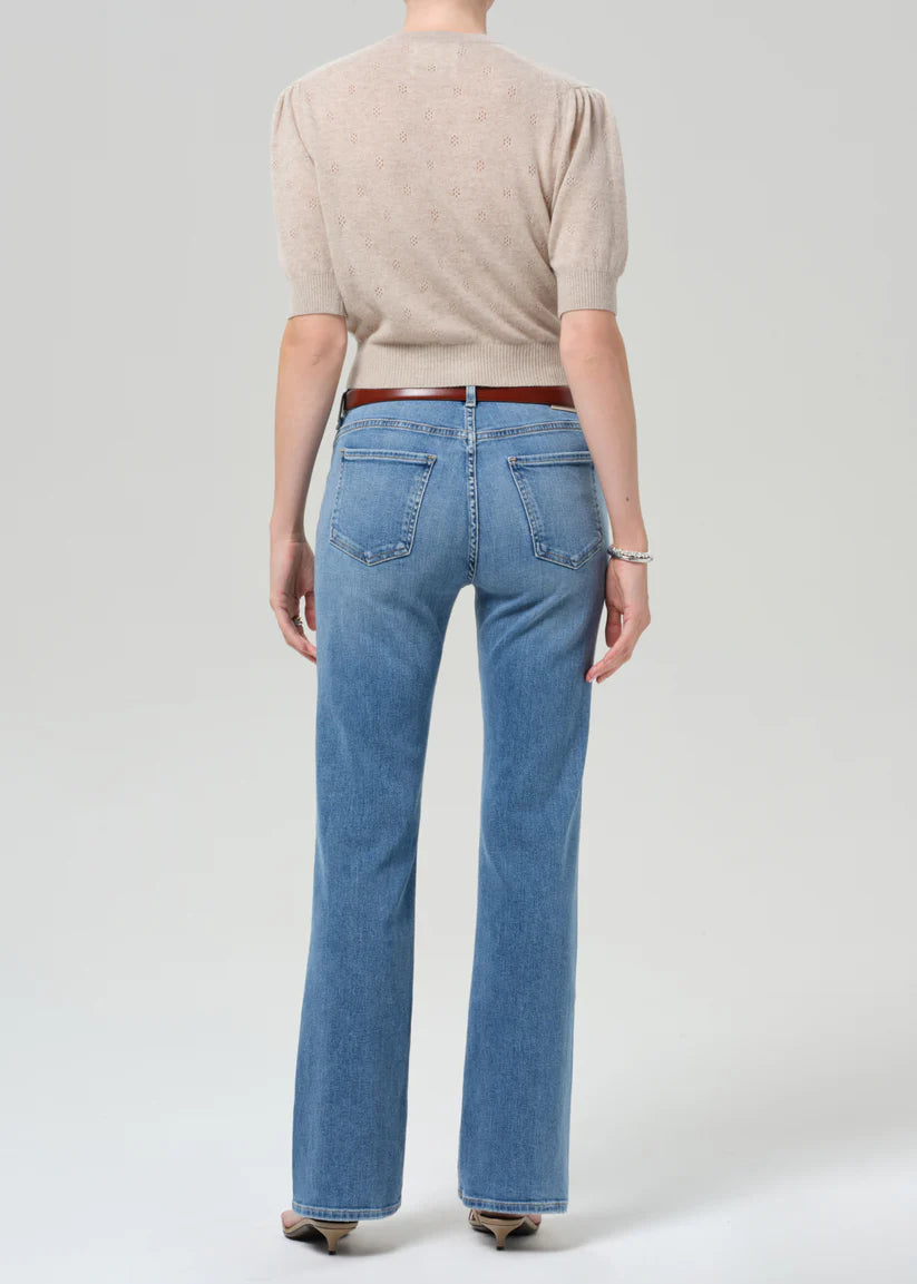 Person wearing blue jeans and a beige sweater on a plain background