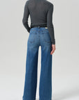 A model shown from the back wearing a dark gray long-sleeve mock neck top and high-waisted, wide-leg blue denim jeans against a light gray studio background.