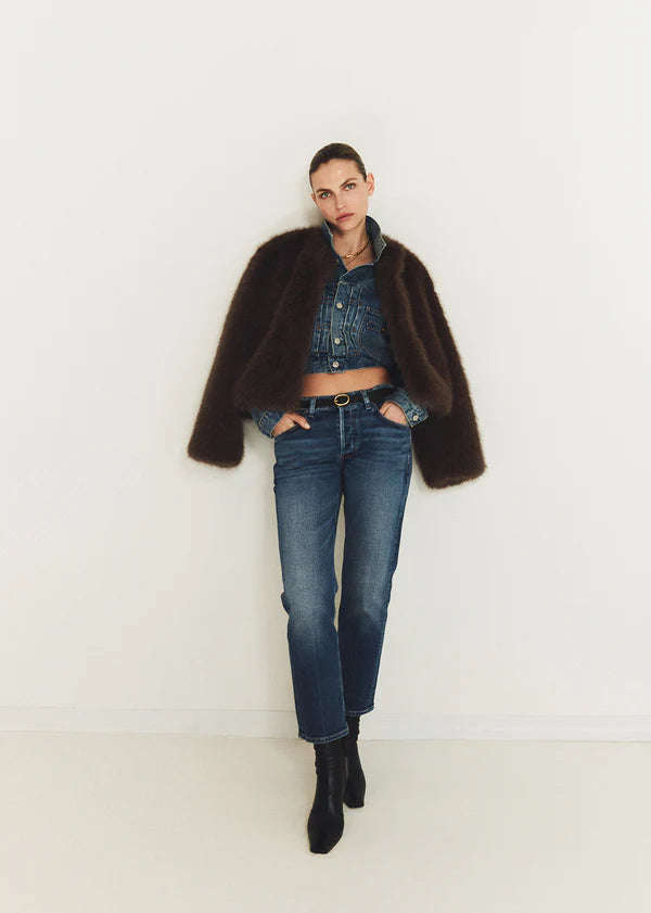 Person wearing a dark brown coat, denim jacket, and jeans standing against a white background front view