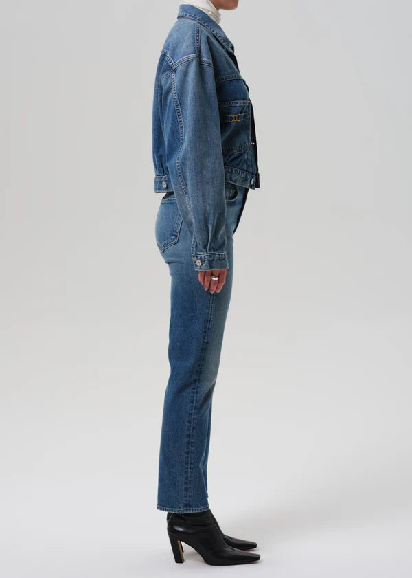 Person wearing a blue denim jacket and jeans on a white background side view
