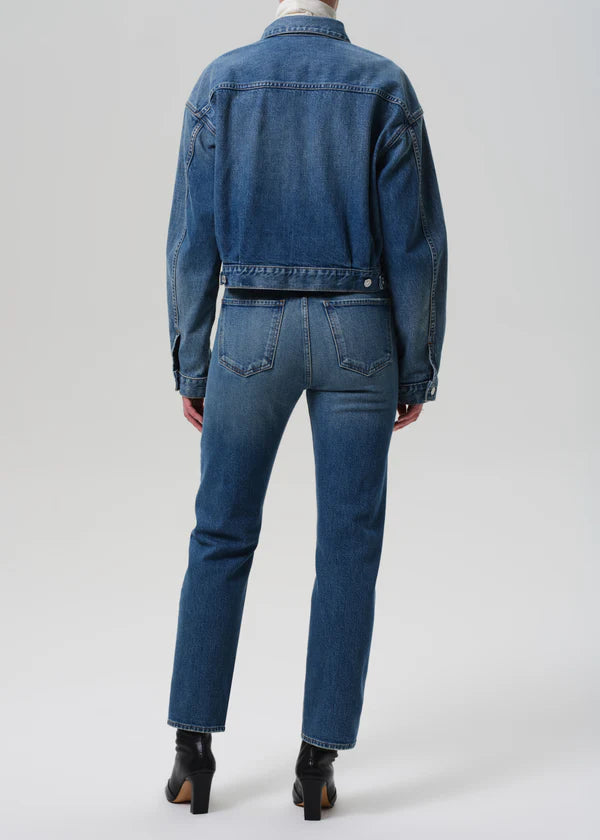 Person wearing a blue denim jacket and jeans on a white background back view
