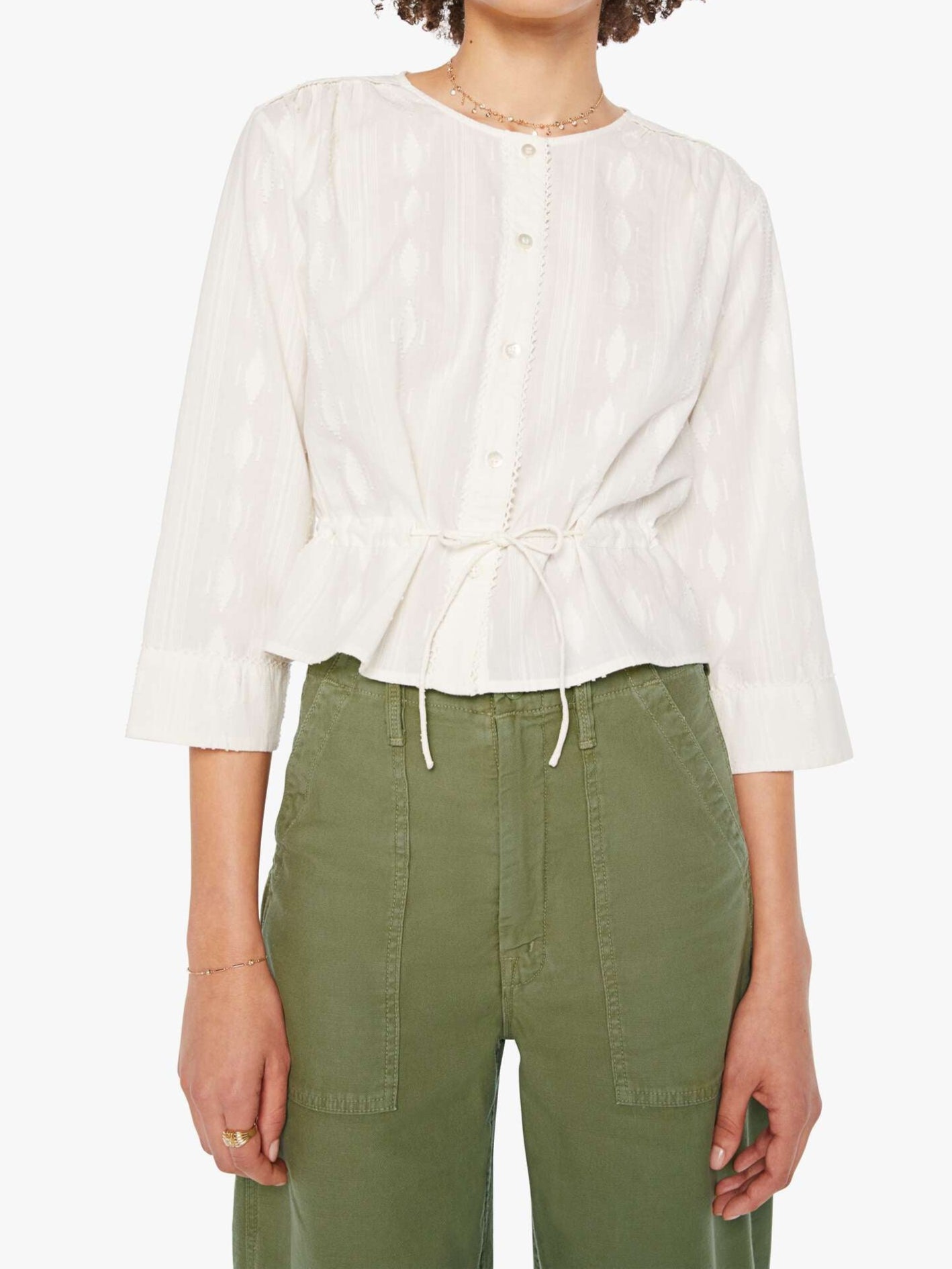 Woman wearing a white blouse with a tie detail and green pants on a white background