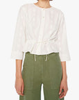 Woman wearing a white blouse with a tie detail and green pants on a white background