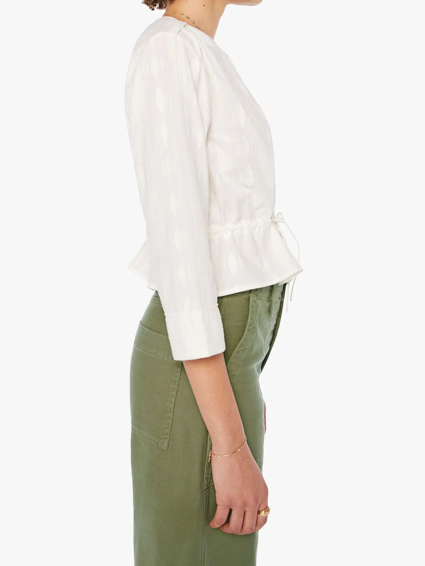 Woman wearing a white blouse and green pants on a white background, side