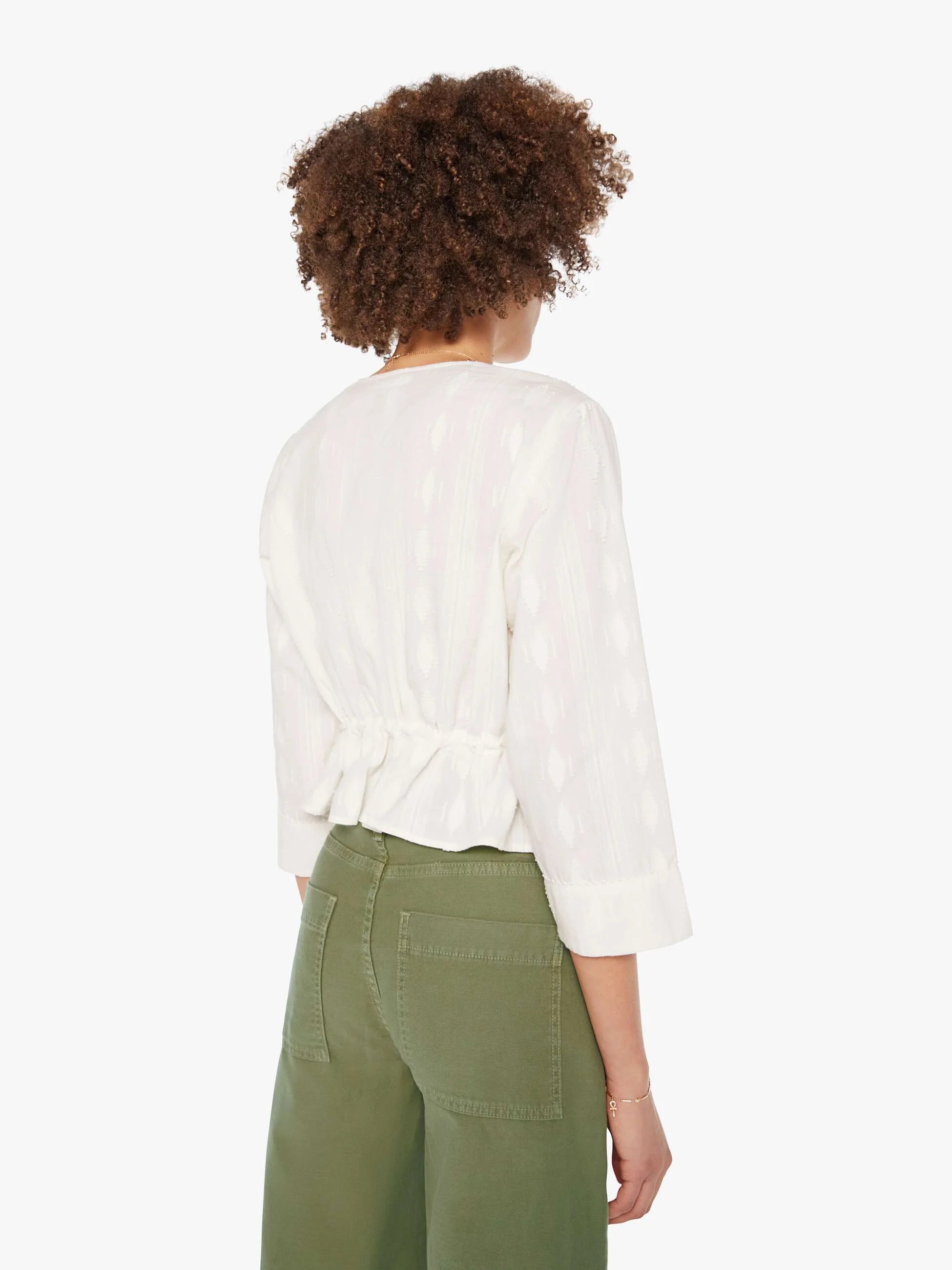 Person wearing a white blouse and green pants on a white background, back