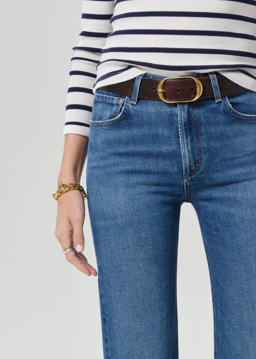 Person wearing a striped shirt and blue jeans with a brown belt on a light gray background