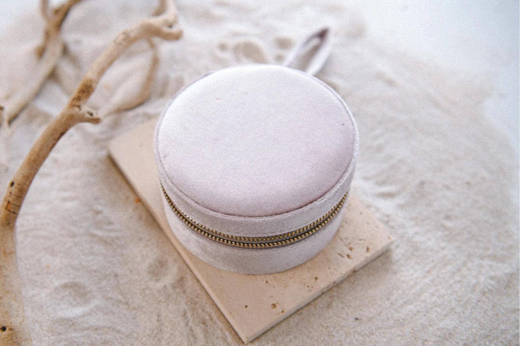Round beige jewelry box with gold zipper on a sandy surface