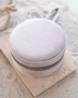 Round beige jewelry box with gold zipper on a sandy surface