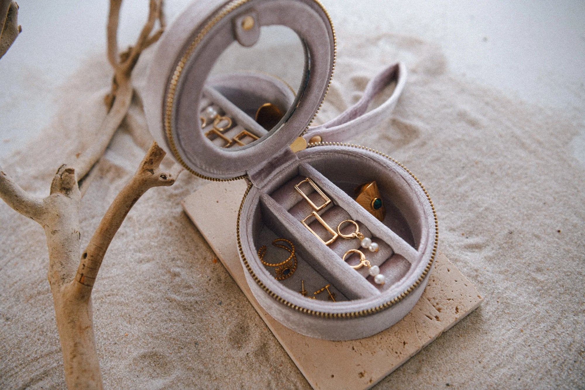 Open jewelry box with gold jewelry on a sandy surface