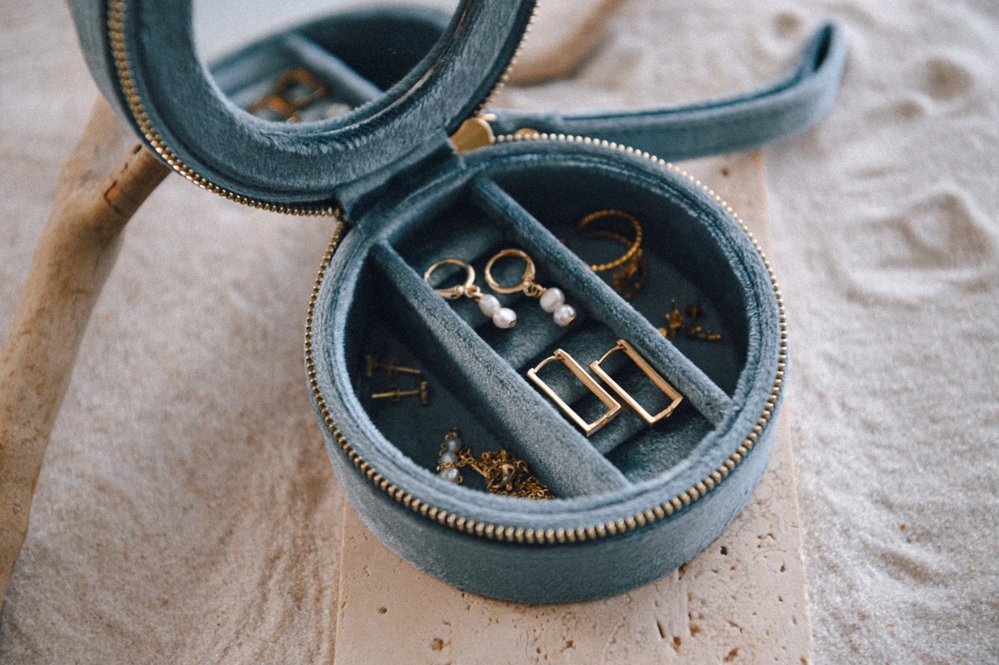 Blue jewelry box with gold jewelry on a textured surface