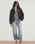 Person wearing a black leather jacket, gray shirt, and light blue jeans on a white background