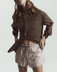 Woman wearing a brown shirt and striped shorts on a plain background