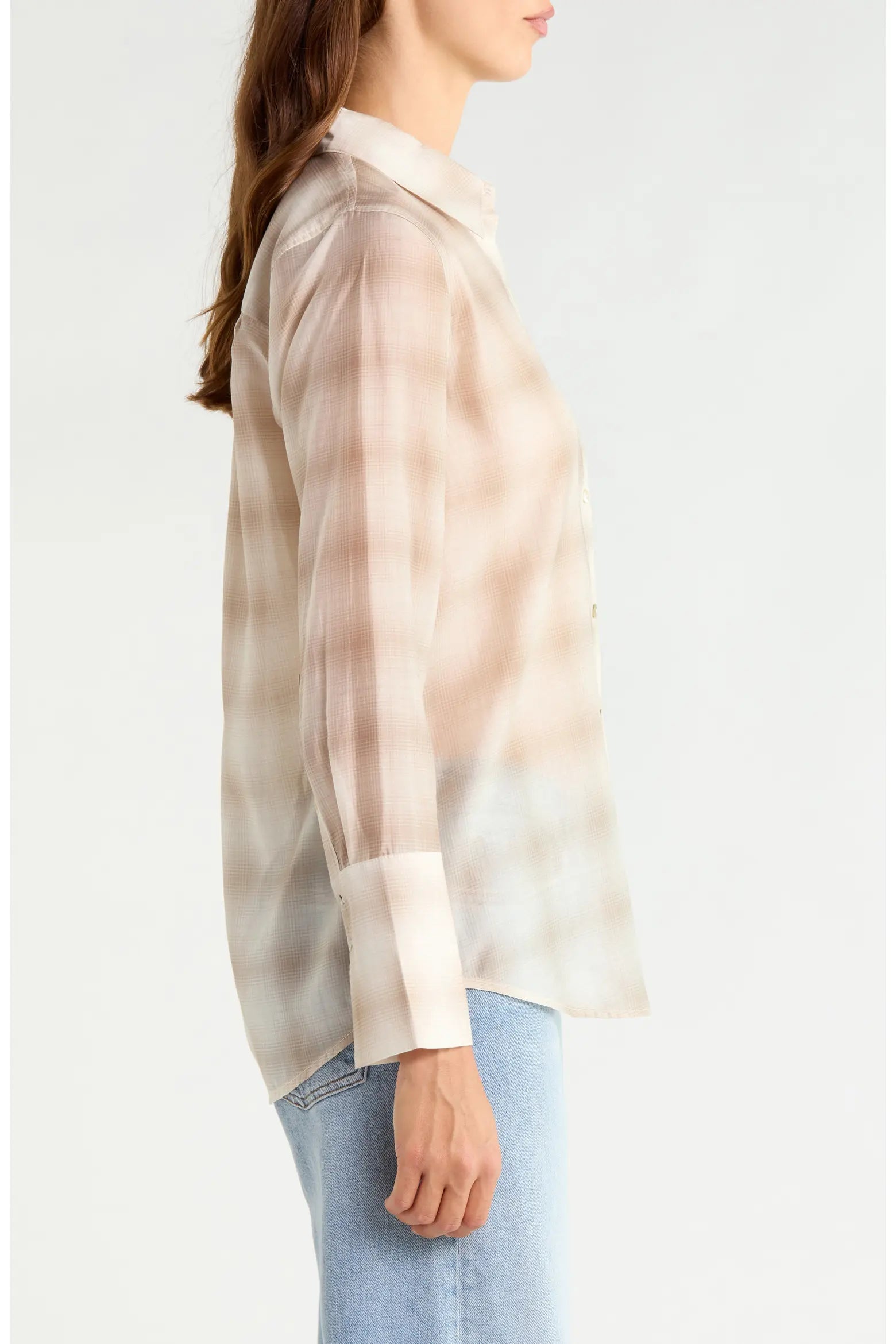 A woman shown in side profile wearing a sheer, long-sleeve button-up shirt with a beige and white plaid pattern, paired with light blue jeans, against a plain white background.
