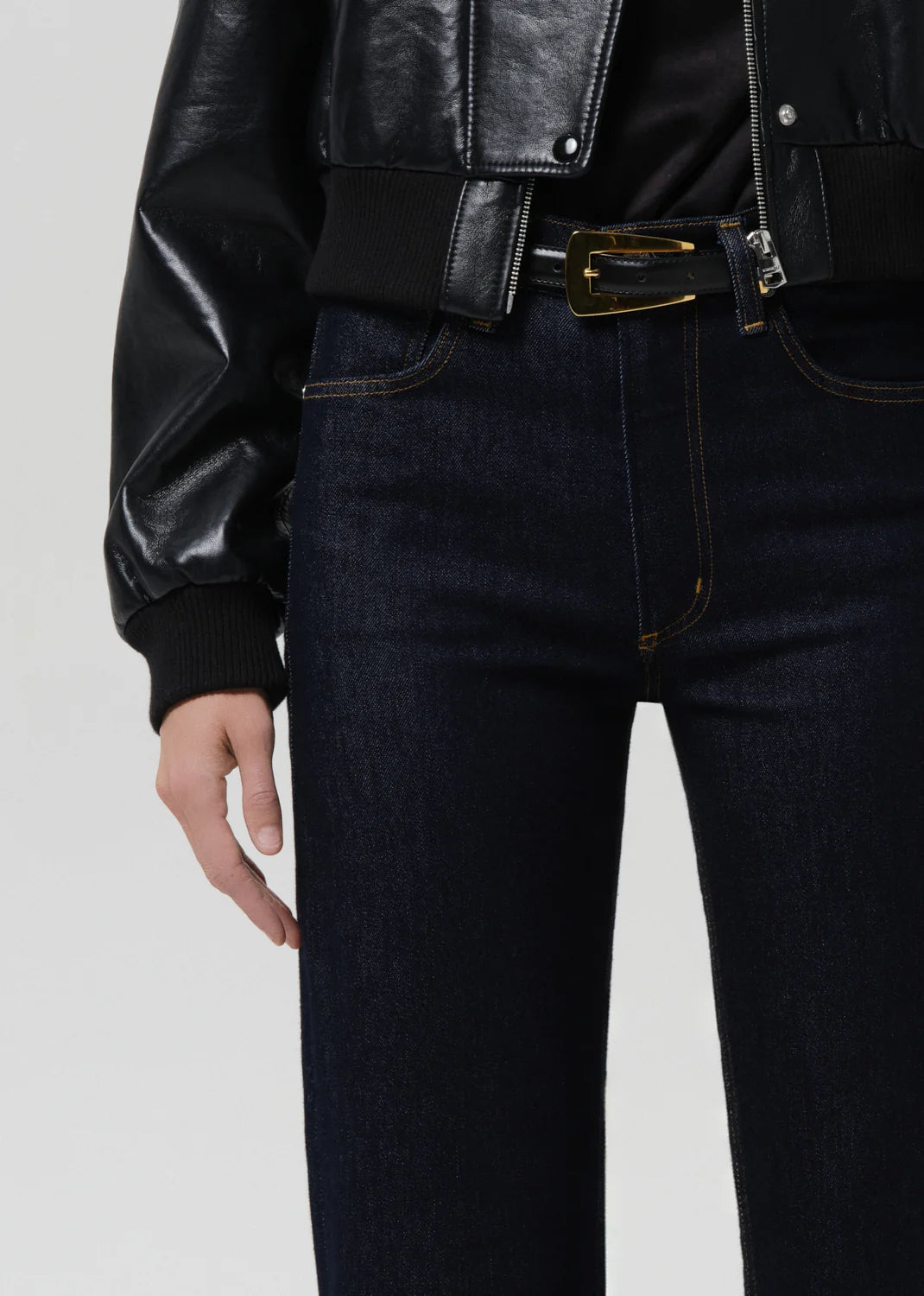 Person wearing a black leather jacket and dark jeans on a light gray background