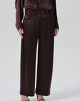 A model wearing dark brown wide-leg trousers with a matching belt and waist tie, paired with a matching dark brown satin long-sleeve top and black strappy heels, against a light gray studio background.