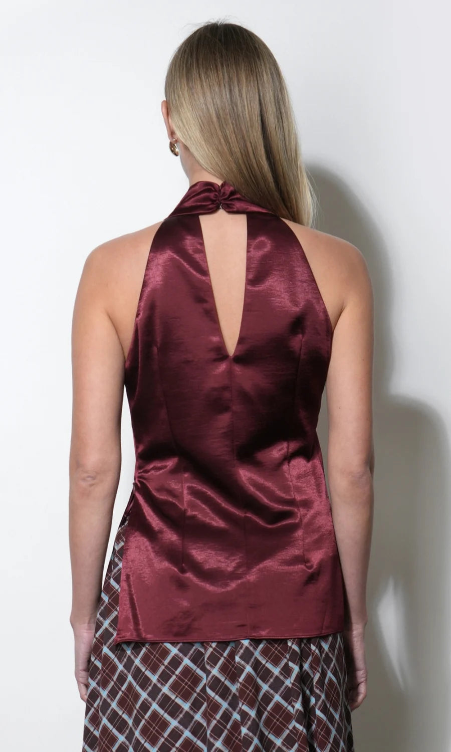 A woman shown from the back wearing a satin halter top in a deep burgundy color, paired with a patterned skirt, against a plain white wall.