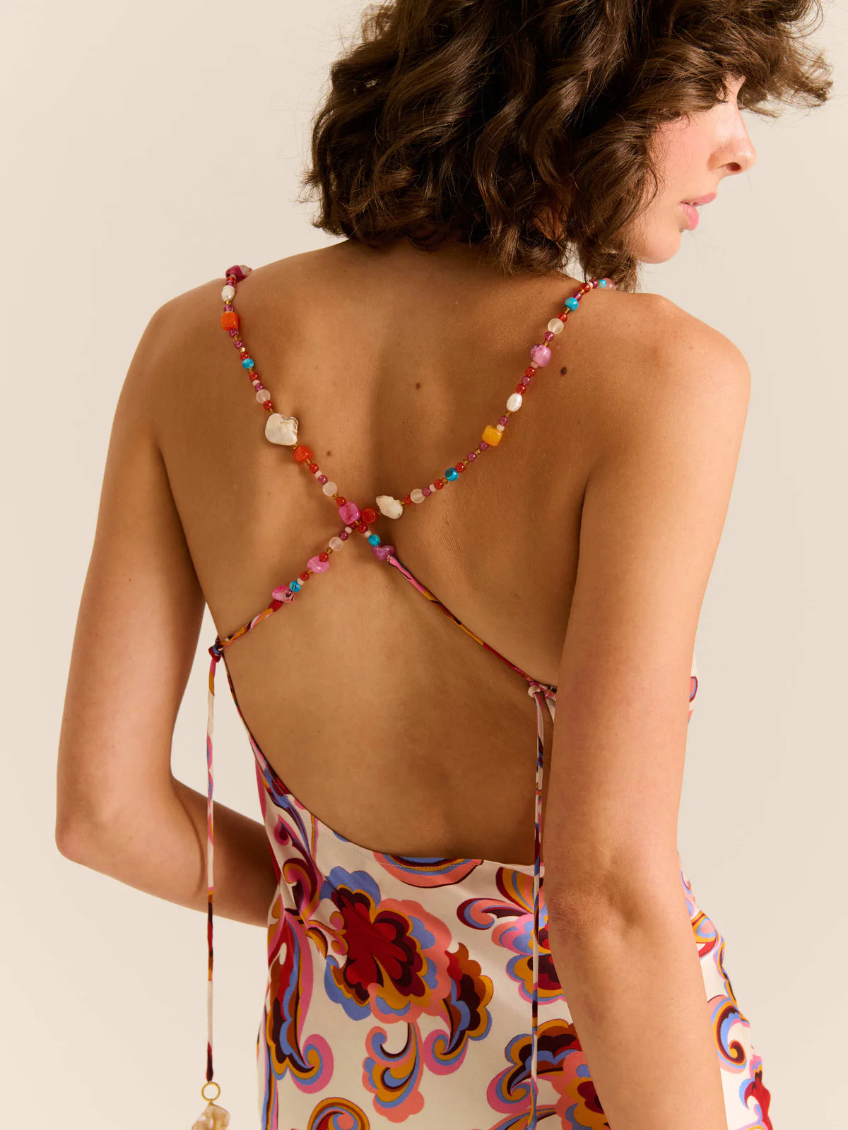 Woman wearing a colorful dress with a beaded back detail on a beige background