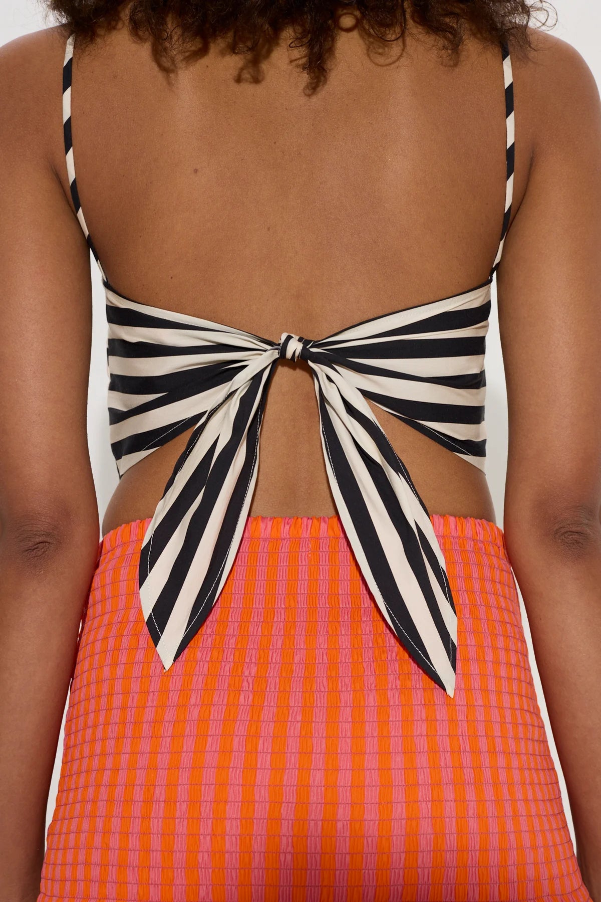 Person wearing a black and white striped top with a bow detail and an orange checkered skirt.