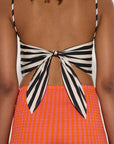 Person wearing a black and white striped top with a bow detail and an orange checkered skirt.