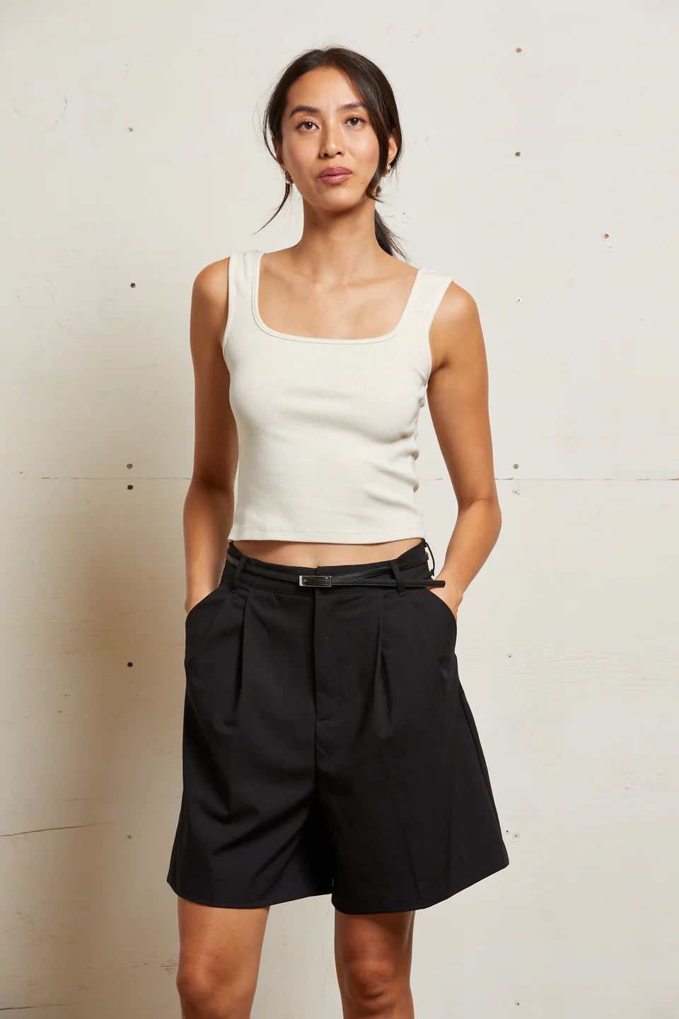 Woman wearing a white tank top and black shorts against a plain background front view