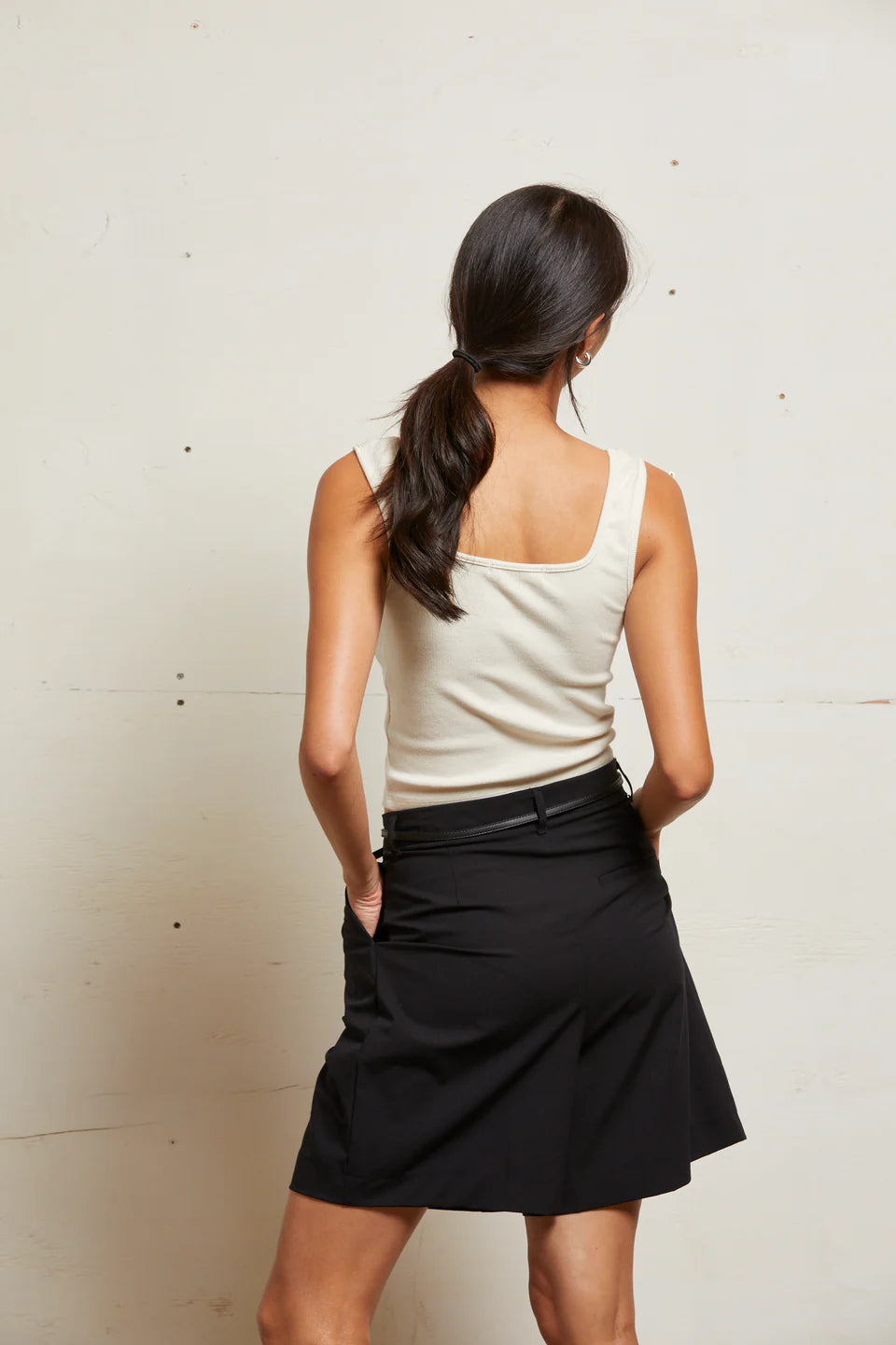 Woman wearing a white top and black skirt against a plain background back view
