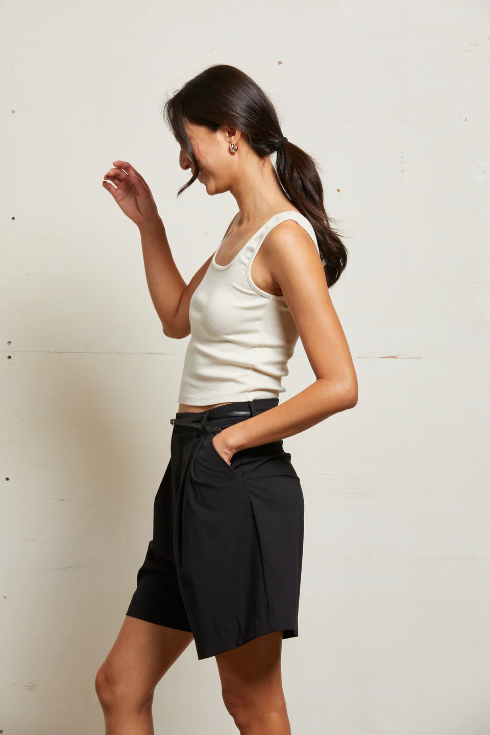 Woman wearing a white tank top and black skirt against a plain background side view