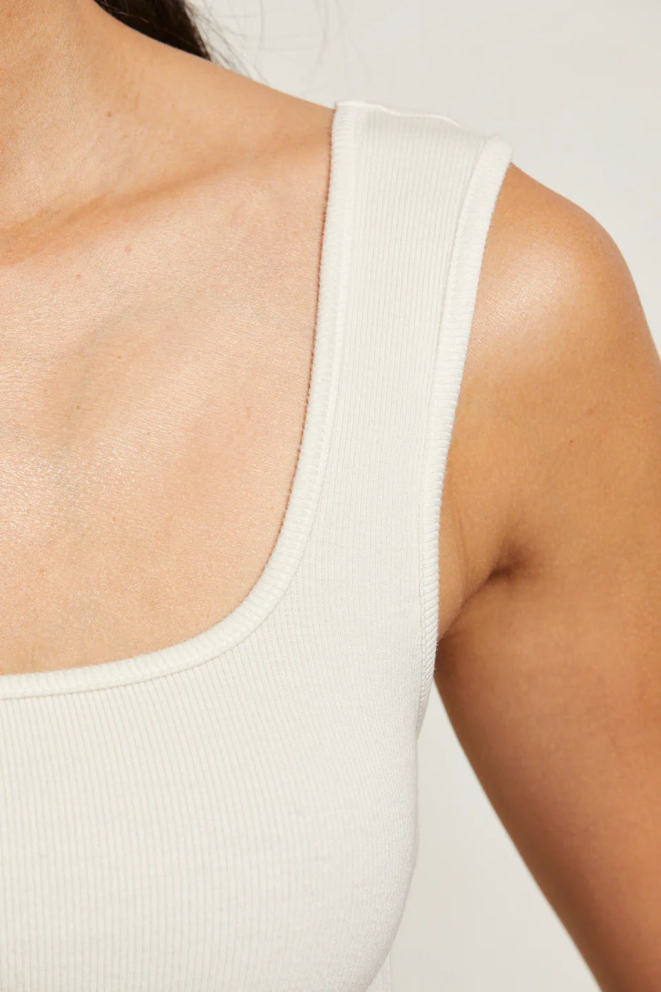 Close-up of a person wearing a white tank top against a neutral background detail view