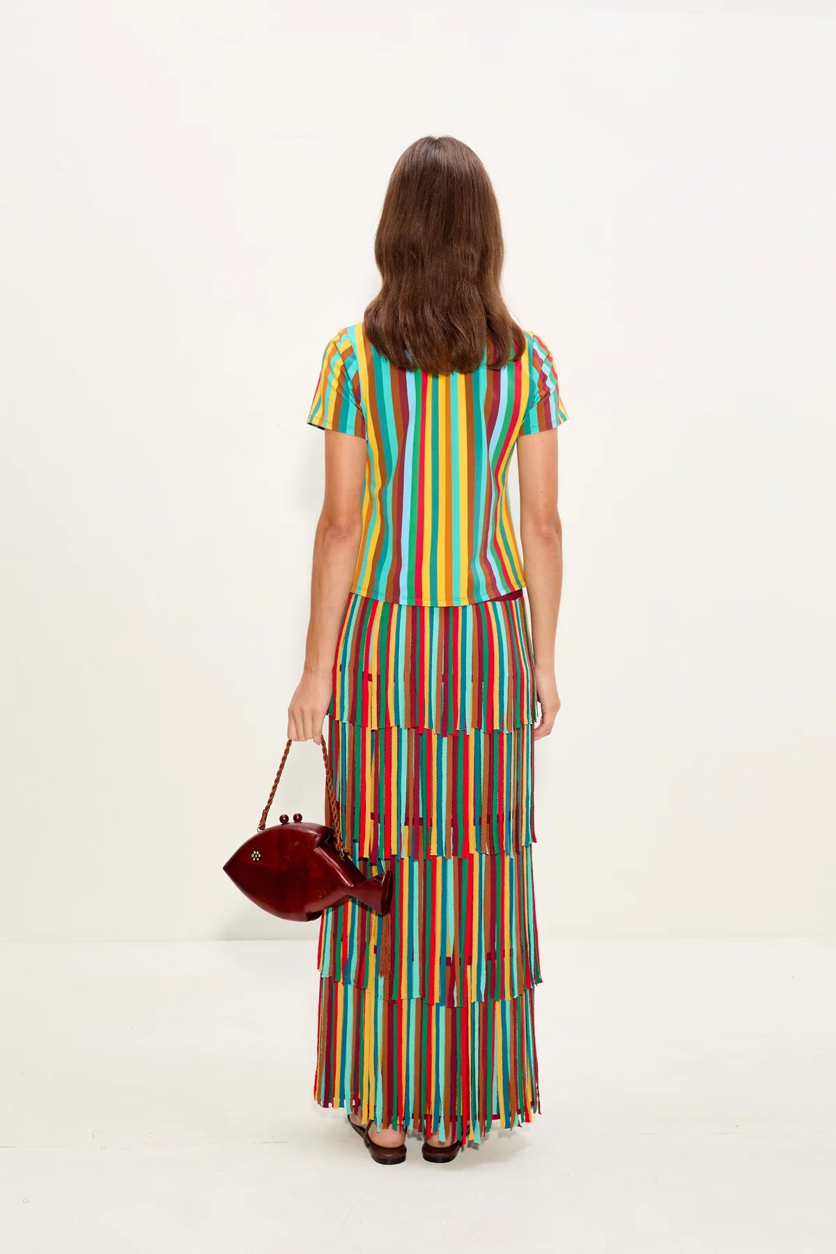 Woman wearing a colorful striped skirt holding a red handbag on a white background