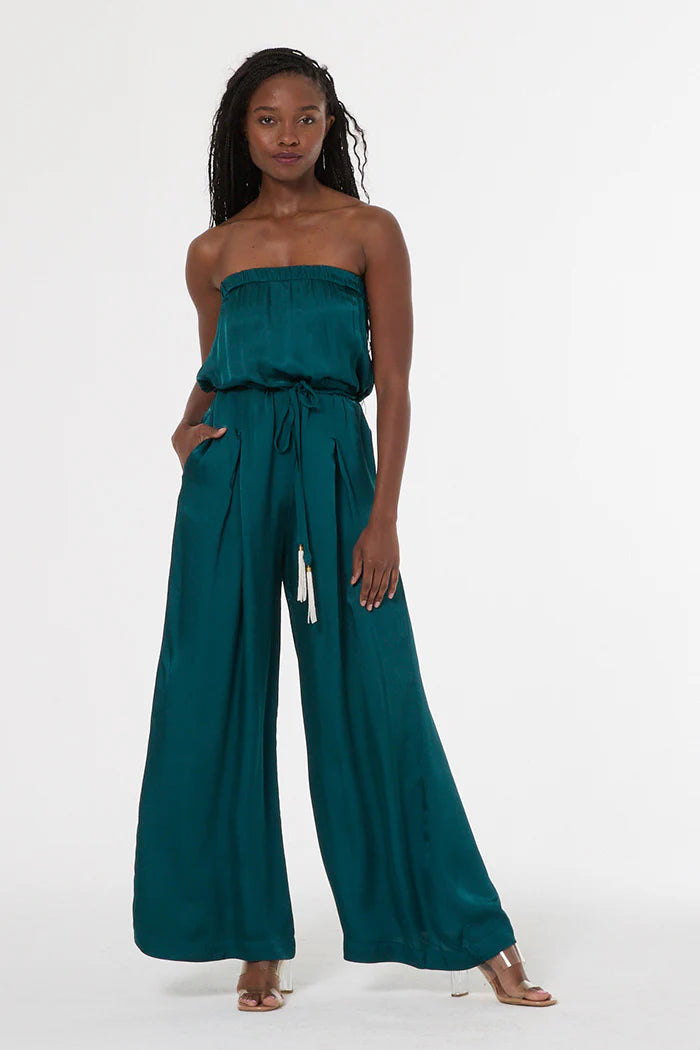 Woman wearing a teal strapless jumpsuit on a white background