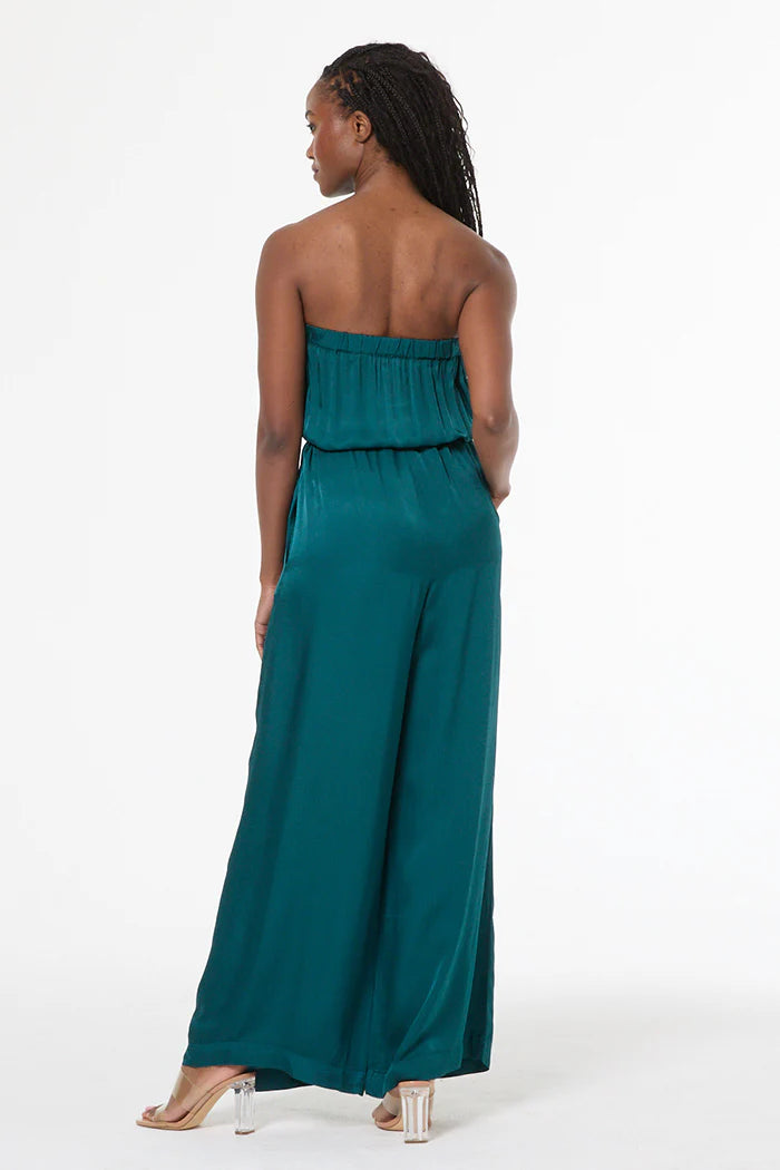 Woman wearing a teal strapless jumpsuit on a white background