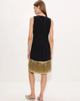 A woman shown from the back wearing a sleeveless black dress with a textured, fringed gold hem, paired with gray pointed-toe mule heels, against a plain white studio background.