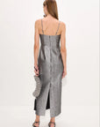 A woman shown from the back wearing a metallic silver spaghetti-strap midi dress with a textured pattern, holding a matching silver clutch, against a plain white studio background.