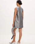 A woman shown from the back wearing a sleeveless silver textured mini dress, holding a matching silver patterned clutch, and wearing silver pointed flats against a plain white studio background.