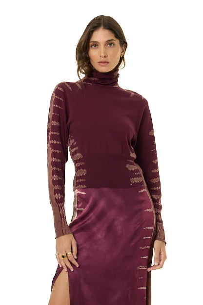 A woman modeling a long-sleeve turtleneck dress in deep plum purple, featuring sheer patterned sleeves and a satin-like skirt, against a plain white background.