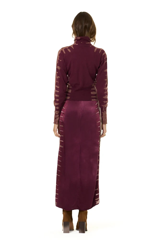 A model shown from the back wearing a long-sleeve turtleneck top and matching maxi skirt set in a deep burgundy color, featuring textured side panels, on a solid white background.