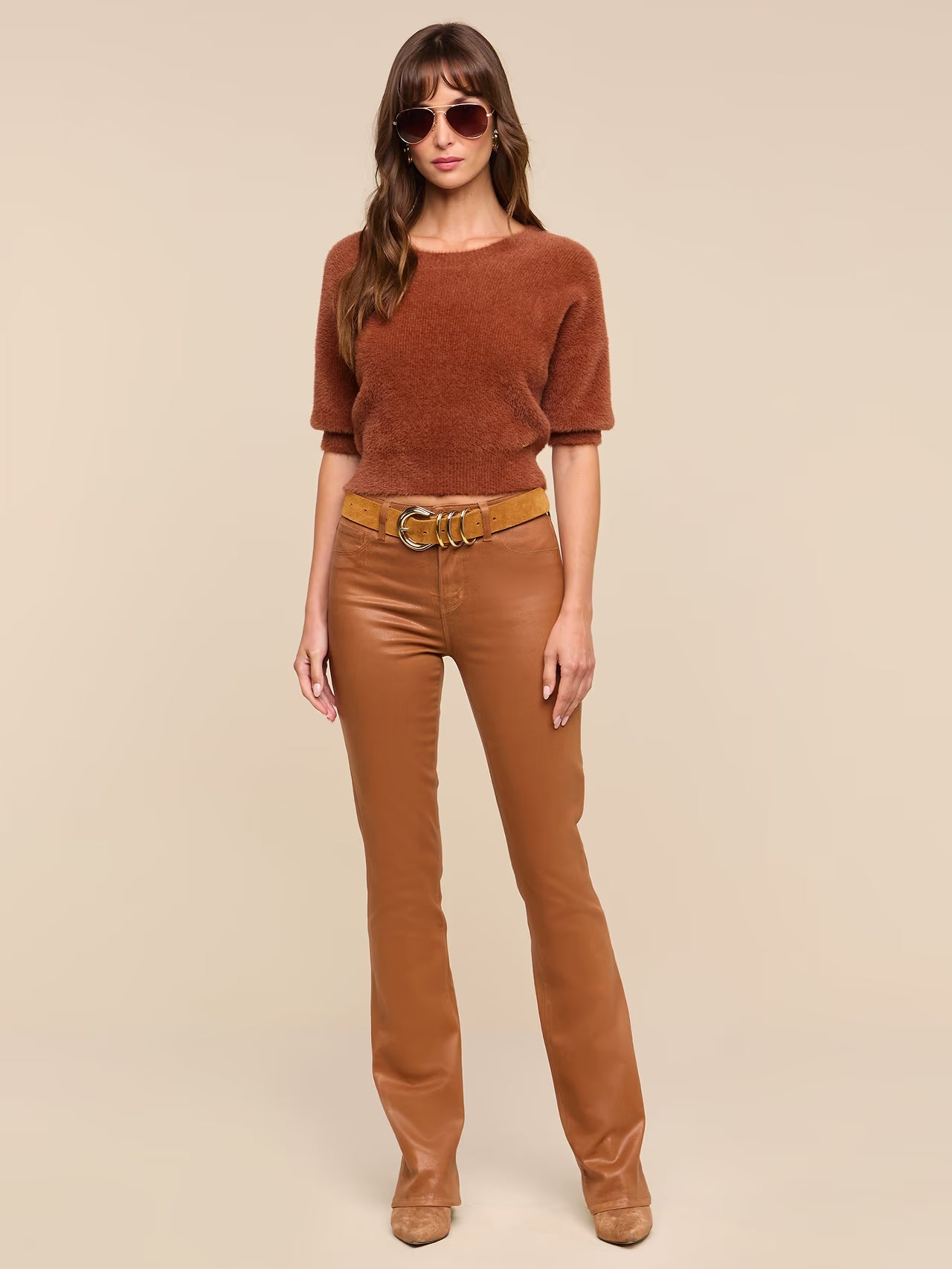 A woman modeling a brown short-sleeve knit top and matching brown pants with a wide brown belt, photographed against a plain beige studio background.