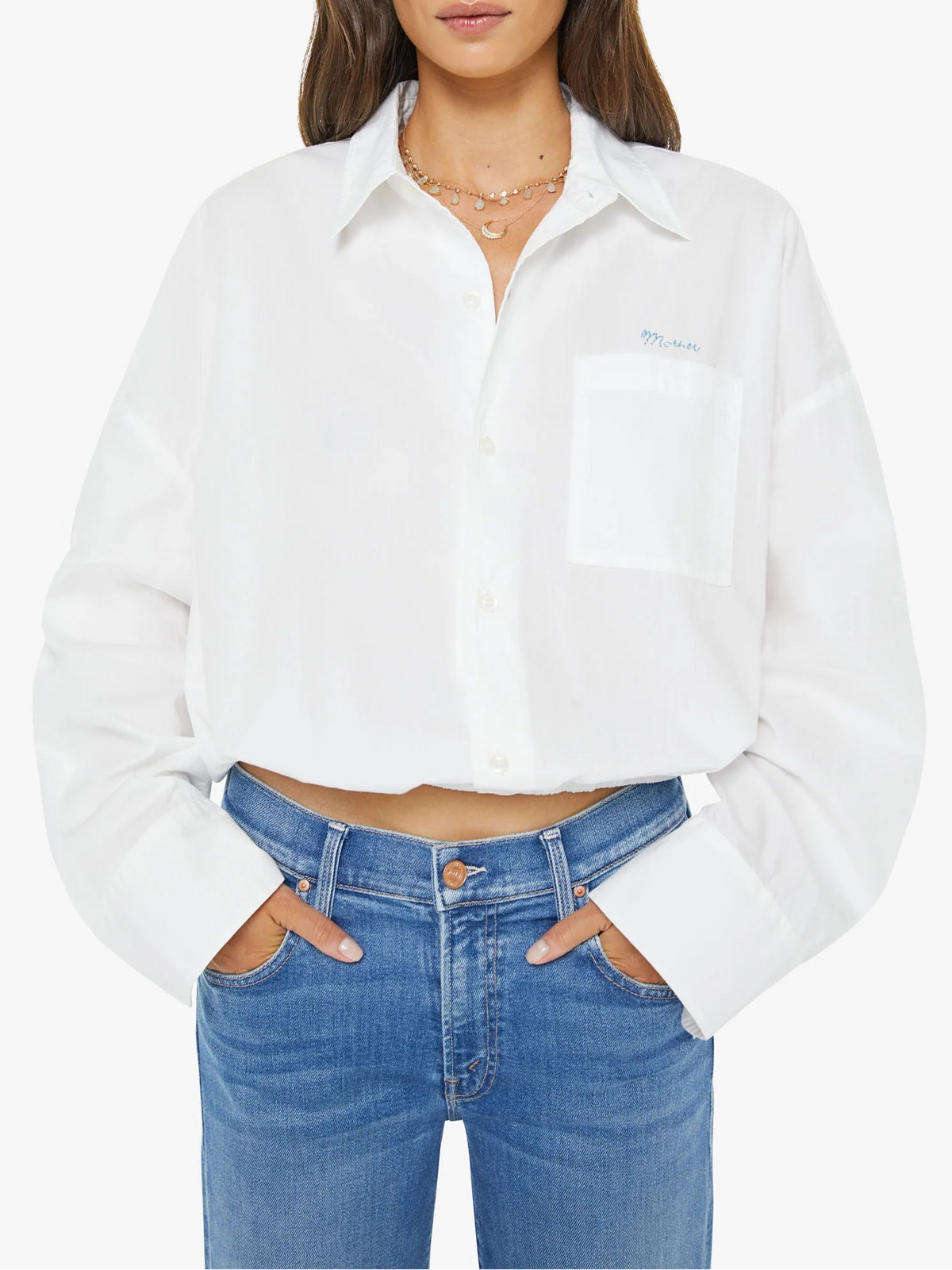 A woman modeling a white cropped button-up shirt with a chest pocket and light blue jeans against a plain white studio background.