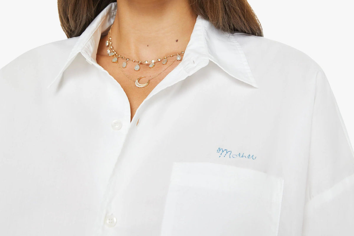 Woman wearing a white shirt with a visible brand logo on a plain background
